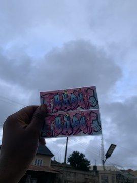 A hand holds up a graffiti-style sticker reading 'NO MORE LIES' against a cloudy sky with buildings below.