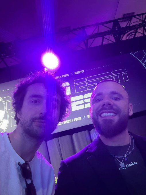 Selfie of two smiling young men at an ESPN event with purple lighting, with one wearing a white shirt and the other wearing a black shirt featuring an 'Aria_Grakes' logo.