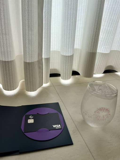 A purple Visa card rests on a black envelope beside a glass of ice water, evoking a premium hospitality welcome for the "Luxe crew."