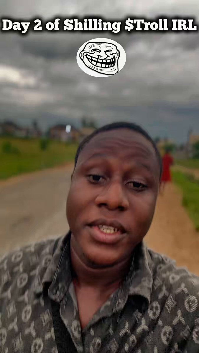 The image shows a man posing for a picture with a smile while wearing a shirt that says $Troll. The caption of the photo reads, "Day 2 of shilling $Troll, but this time outside campus. I gave the Troll meme face to few individuals at the pharmacy, a nearby hostel, cyber cafe and my barber's shop Love how they responded by saying ...". This is an example of a meme that features a humorous graphic or text about the topic "Day 2 of shilling $Troll", which seems to be related to the person taking the photo. The caption suggests that someone enjoys the humor in this scenario, and it appears that others may share their opinion as well.