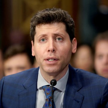 A man with short brown hair, wearing a navy blue suit jacket, light blue shirt, and patterned tie, speaks at a microphone during what appears to be a formal hearing or press event, with blurred figures visible in the background.

The image appears to show Sam Altman, CEO of OpenAI, in connection with the news that OpenAI has fired three safety researchers for allegedly sharing sensitive information with an outside group.
