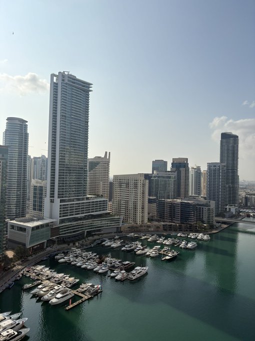 A scenic waterfront cityscape featuring modern high-rise towers overlooking a marina filled with docked yachts and boats along a calm blue bay. The "GM 💙" post likely expresses appreciation for the urban beauty captured in this Miami-like skyline view.