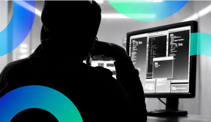 Silhouette of a hooded figure looking at a computer monitor with code, with blue circular graphics overlaid.