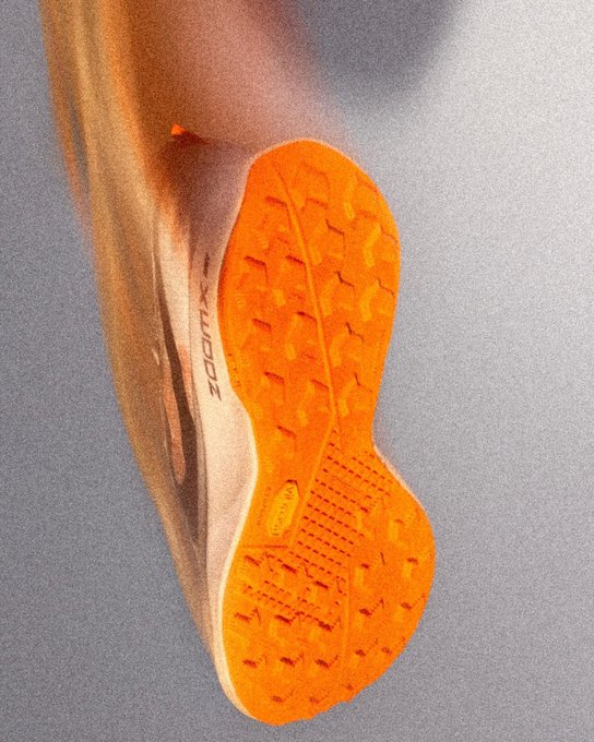 A close-up of the orange Vibram outsole and ZoomX branding on the sole of a running shoe, shown against a gray background.
