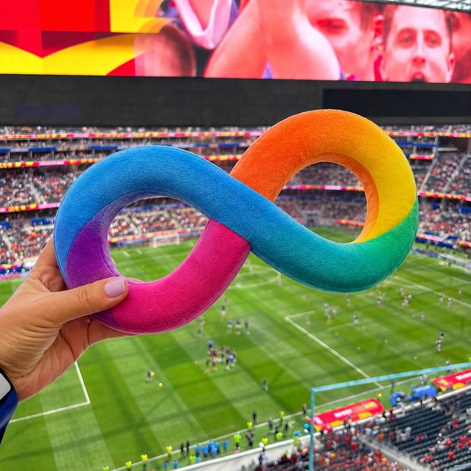 A hand holds a colorful infinity-symbol-shaped foam pillow in the foreground, with a crowded soccer stadium and a large screen in the background, while the post promotes "$ICP," likely referring to Internet Computer Protocol, tying the vibrant, forward-looking imagery to enthusiasm for the cryptocurrency.