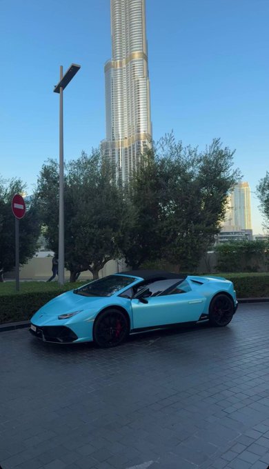 A blue Lamborghini convertible is parked on a tiled plaza with the Burj Khalifa towering in the background, embodying the post's "GM to everyone who says GM" flex with ultimate style and luxury.