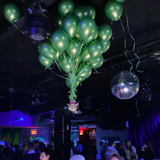A nightclub scene features a large cluster of green balloons floating above a disco ball and crowd, with neon lighting and an EXIT sign visible.