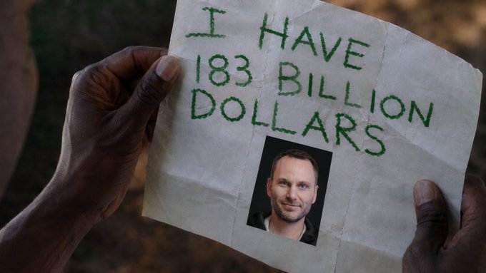 Dark-skinned hands hold up a torn paper sign that reads 'I HAVE 183 BILLION DOLLARS' in green stitched text, with a photo of a smiling man pasted below the text.