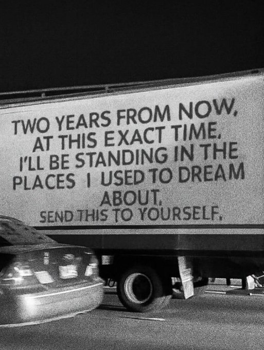 A black-and-white photo of a truck on a highway displaying a billboard that reads: 'TWO YEARS FROM NOW, AT THIS EXACT TIME, I'LL BE STANDING IN THE PLACES I USED TO DREAM ABOUT. SEND THIS TO YOURSELF.'