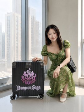 A woman in a green dress posing next to a black suitcase labeled "Dungeon Saga" featuring a pink crest design.