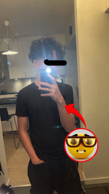 A mirror selfie of a young man in a black t-shirt holding a phone with the flash on, with a smiley face emoji wearing sunglasses edited in via a red arrow.