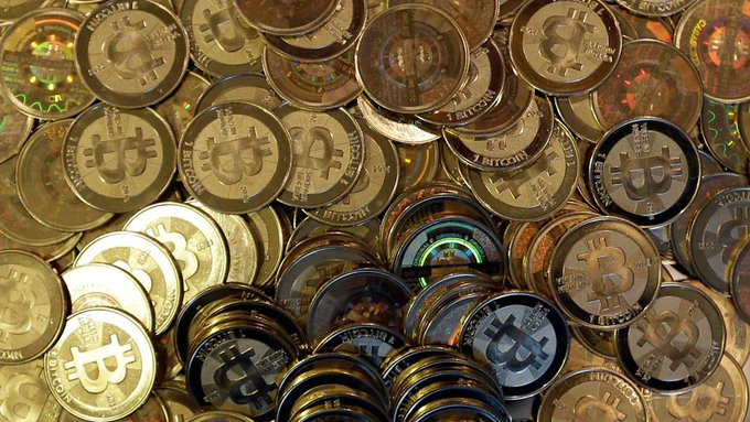 A pile of shiny physical Bitcoin coins with various cryptocurrency designs stamped on them.