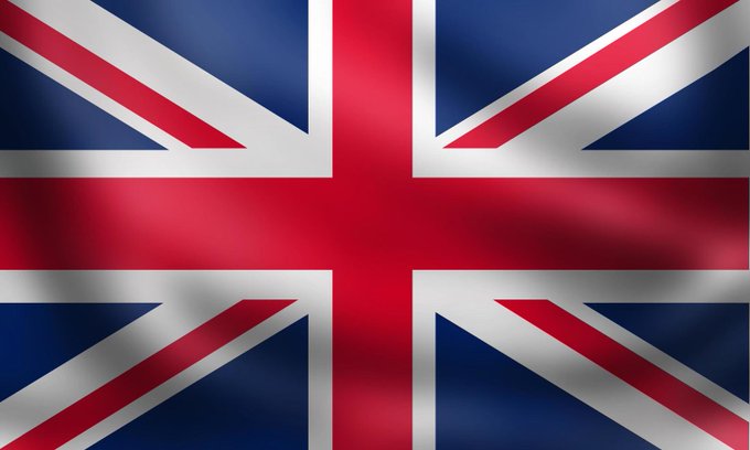 The image shows a close-up of the Union Jack (UK flag) with its characteristic red, white, and blue colors in a waving fabric appearance. It accompanies news about the UK's Financial Conduct Authority preparing new regulations for tokenized gold, visually symbolizing Britain's prominent role as the world's largest over-the-counter gold trading center, handling approximately 70% of global notional gold volume, primarily through London.