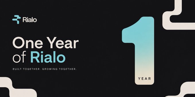 A promotional banner for 'Rialo' celebrating 'One Year of Rialo' with the subtitle 'BUILT TOGETHER. GROWING TOGETHER.' featuring a large '1' marking one year.