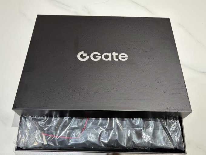A black presentation box branded with the 'Gate' (Gate.io) logo on top, containing a plastic-wrapped item, sitting on a marble countertop.