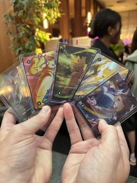 A person's hands holding a fan of several holographic Pokémon trading cards.