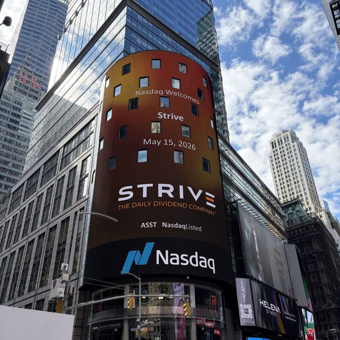 A tall building features a large digital billboard announcing 'Nasdaq Welcomes Strive May 15, 2026' for 'STRIVE THE DAILY DIVIDEND COMPANY' (ticker: ASST), with the Nasdaq logo displayed below.
