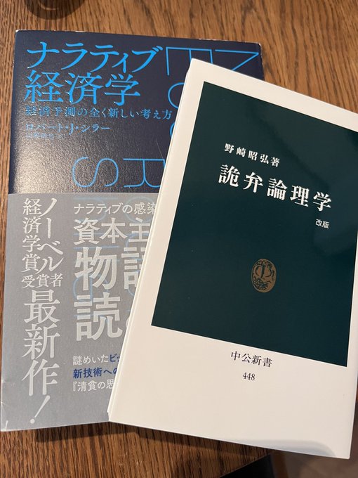 Two Japanese books photographed on a wooden surface: 'ナラティブ経済学' (Narrative Economics) by Robert Shiller and '詭弁論理学' (Fallacy Logic) by 野崎昭弘 from the 中公新書 series.