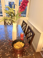 A photo of a dining table with a bowl of tortilla chips and salsa, a can of soda, and a vase with flowers, with petals scattered across the surface.