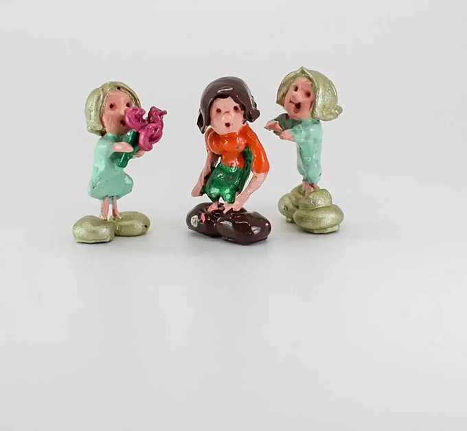 The image features three figurines of children, each with different poses and expressions. One child has a pink flower in their hand, while another one holds a small bird. The third child appears to be holding a toy car or truck. All three figurines are standing on rocks, giving the impression that they might be playing together. The post suggests that these figurines could represent GM guys who are trying to survive and overcome challenges by working together as a team.