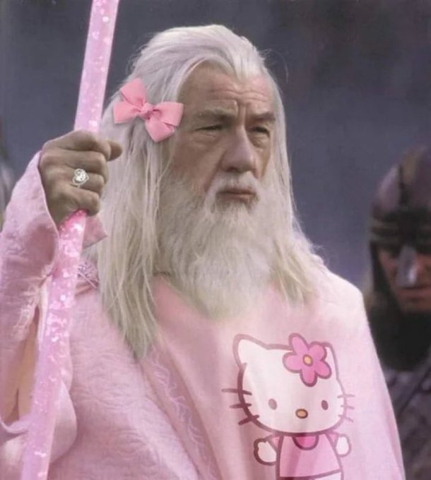 An older man with long white hair and a white beard, resembling the character Odin, is humorously edited to wear a pink Hello Kitty shirt, a pink bow in his hair, and hold a pink staff.