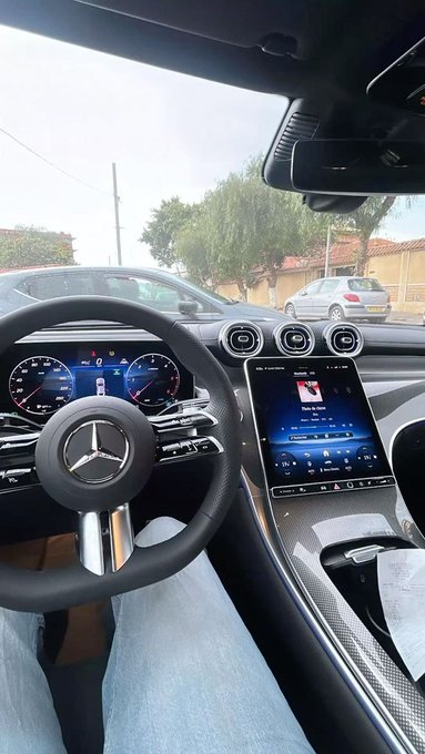 The interior of a sleek Mercedes-Benz is shown from the driver's perspective, featuring a black steering wheel with the iconic three-pointed star logo, a digital dashboard, and a large touchscreen display. The post "Can I get a GM?" plays on the abbreviation, referencing both the car brand visible on the steering wheel and a common phrase.