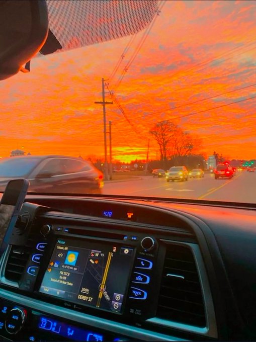 A driver captures a vivid orange sunset while traveling down Derby St, the dashboard clock reading 4:28, creating a striking contrast with the post's message about connecting idle computing power through Quip Network.