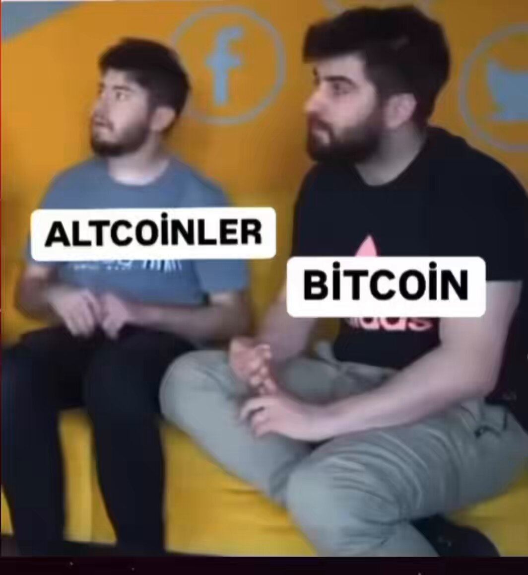 The image shows two men sitting next to each other, both wearing black t-shirts with white text that reads "Altcoinler az birşey yükselince #bitcoin". The background of the image features a yellow wall adorned with various social media icons and logos.