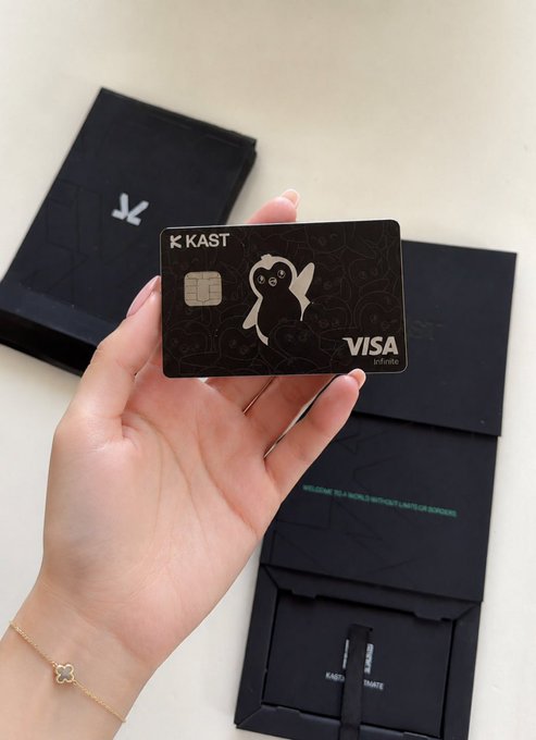 The image shows a person holding up a black Visa card, which has a cute penguin design on it. The card appears to be a KAST Card, as indicated by the text "gKAST! Hold crypto is easy. Actually spending it at the gas station, the café, the grocery store, without jumping through conversion hoops? That'S where most people hit a wall." This suggests that the person might have encountered difficulties while trying to use their card in a non-card reader or payment system and is now sharing their experience with others.