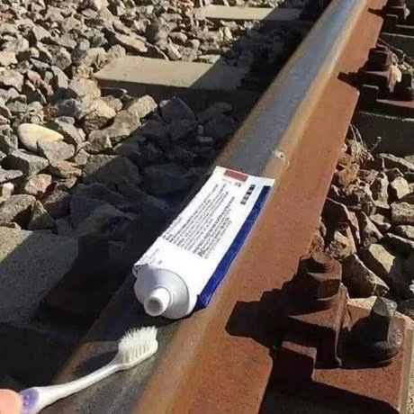 A tube of toothpaste and a toothbrush rest on a rusty railroad track amid gravel, with the post's "Thank you crypto" caption playing on the image's implication of using one's teeth to brush on the tracks—suggesting a tongue-in-cheek reference to someone being left with little more than basic hygiene supplies after a crypto loss.