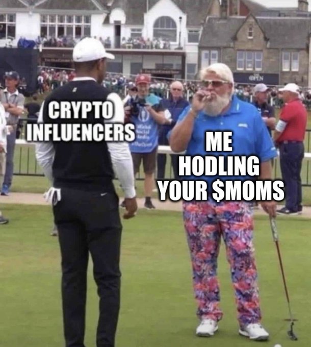 A meme image at a golf event labeling a Black caddie as 'CRYPTO INFLUENCERS' and an older white golfer in floral pants as 'ME HODLING YOUR $MOMS'.