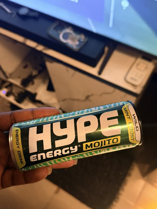 The image features a can of Hyper Liquid energy drink being held by someone's hand. The person is standing next to a television screen or monitor that has a blue background with white lines. The TV appears to be turned off, as there are no visible images on the screen.