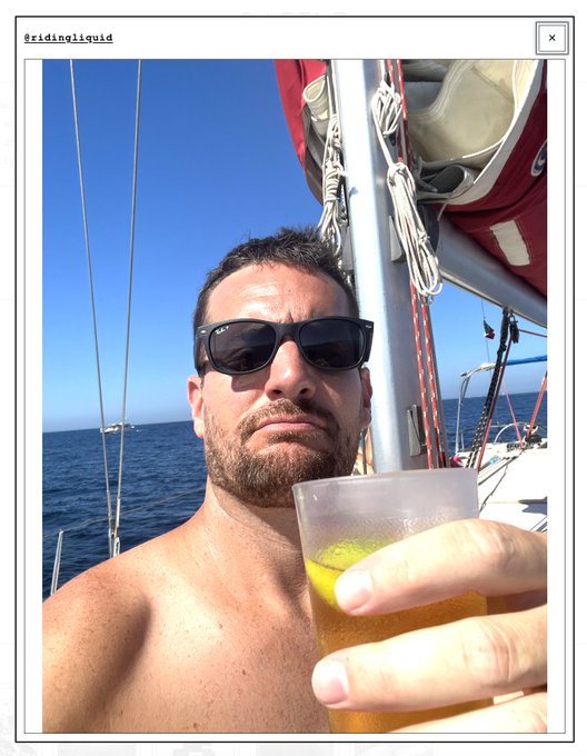 A shirtless man wearing sunglasses taking a selfie on a sailboat while holding a drink, posted by user @ridingliquid.