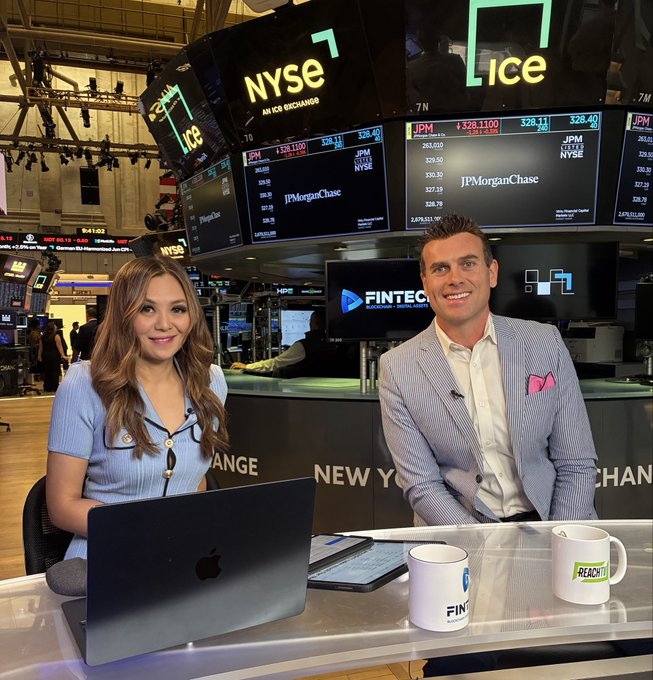 Two news anchors from FinTech.tv broadcasting from the New York Stock Exchange floor, with JPMorgan Chase stock data displayed on screens behind them and 'NYSE' and 'ICE' signage visible.