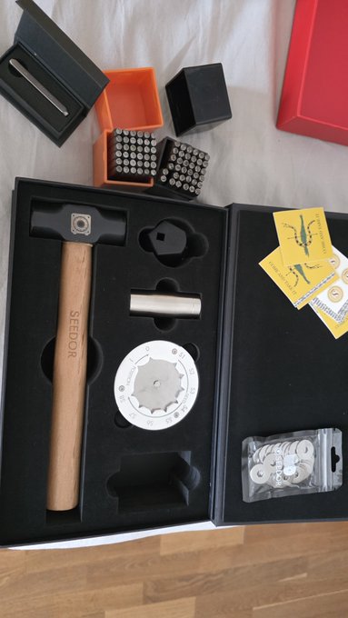An unboxed SEEDOR hammer set displayed in black packaging, featuring a wooden-handled hammer, metal components, storage containers with pin arrays, drill bits, and yellow instruction cards.