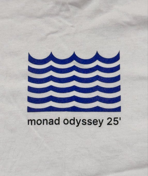 A close-up of a white t-shirt featuring a blue wavy lines logo above the text 'monad odyssey 25'' in black lowercase letters.