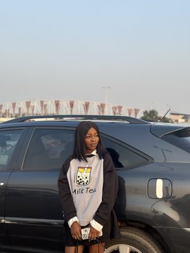 In the image, there's a woman standing next to her black SUV car. She is wearing a long-sleeved shirt with a graphic design of a cupcake on it, and she also has a purse slung over her shoulder. The text in the post reads "This is me before and after I became a @doginaldogs". It seems that the woman's journey from being identified as a doginal to becoming a human has been captured in this photo.
