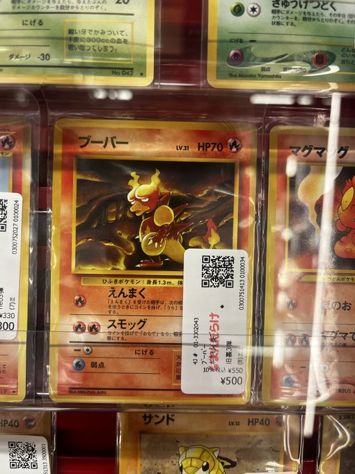 A Japanese Pokémon trading card display showing a holographic Magmar card (LV.31, HP70) priced at ¥500, with other cards visible including Dodrio and Sandshrew, each with QR code price tags.