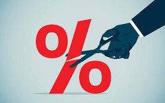 A graphic illustration shows a hand in a suit holding scissors cutting through a large red percent (%) symbol against a light teal background, symbolizing rate cuts.