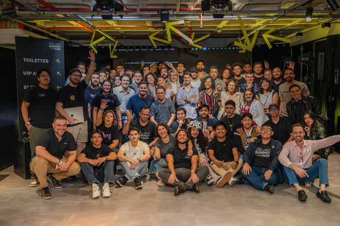 A large group photo of dozens of people posing together indoors at what appears to be a gaming or esports venue, with some wearing 'Summer Game Fest' shirts and signs visible for 'TOILETTES' and 'VIP A'.