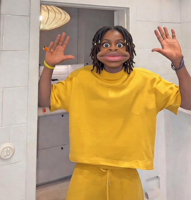 A young person wearing a yellow t-shirt and sweatpants, using a face filter that distorts their features for a humorous effect while posing with hands raised.