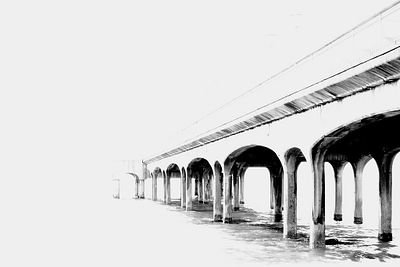 A black and white sketch or drawing of a long bridge or pier with arched supports extending into a blank white background.