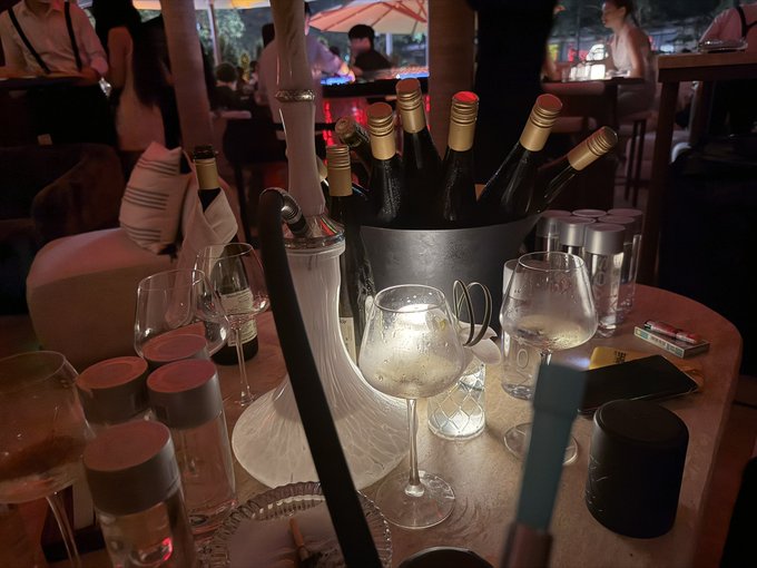 A dimly lit restaurant table featuring a wine bucket with bottles, empty wine glasses, and a white sculptural centerpiece.