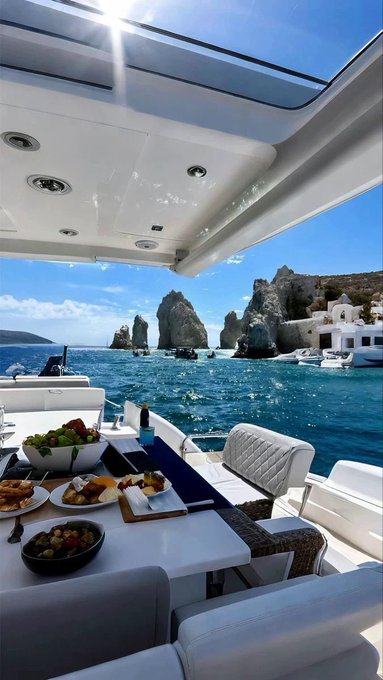 A luxurious yacht setting features a dining table laden with fresh fruit and appetizers, overlooking turquoise waters and dramatic rocky cliffs in the background. The serene, high-end maritime scene contrasts with the post's message about crypto projects @RiverdotInc and @NomismaNetwork advancing Web3 finance, though there is no direct visual connection to the blockchain content.