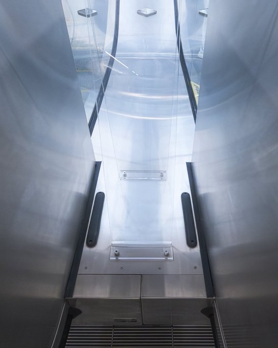 A view looking up from inside a sleek, metallic elevator shaft with glass panels revealing a bright sky above. The futuristic, almost sci-fi setting complements the "Good night!" message, suggesting a final upward journey or a dreamlike transition into rest.