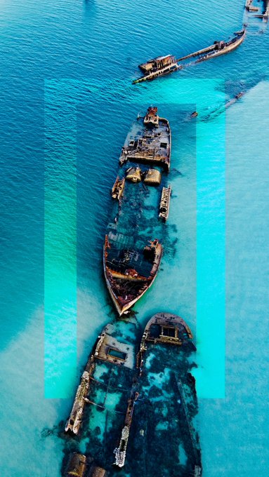 An aerial drone view of rusted shipwrecks in clear turquoise water, with a translucent blue and pink rectangle overlaid on the center of the image.