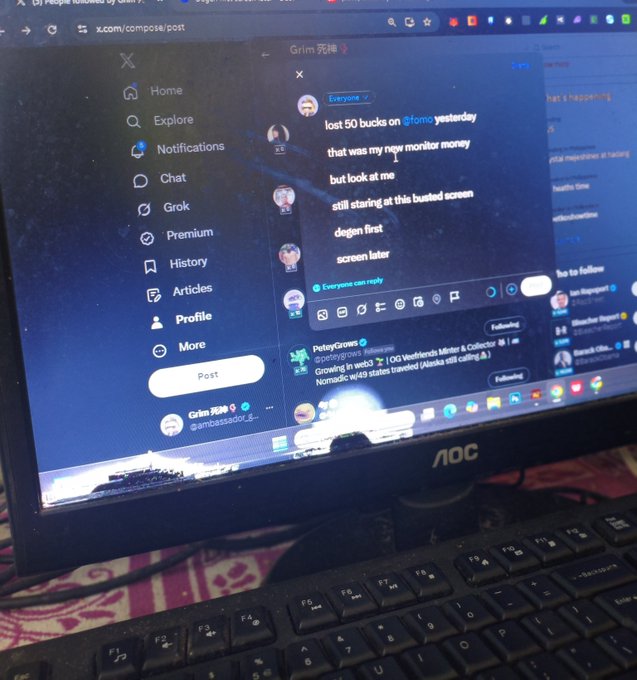 A photograph of an AOC computer monitor showing a Twitter/X post by 'grim' (@anairbassadorjr) complaining about losing $50 and needing a new monitor, with a keyboard visible in the foreground.