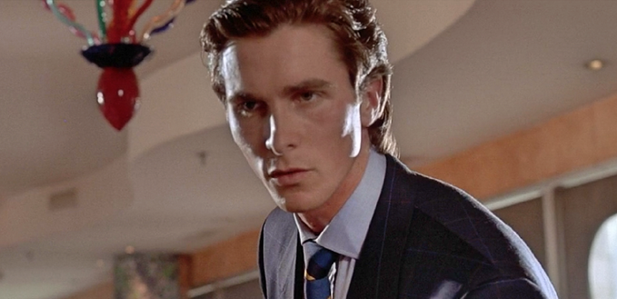 A still from the movie American Psycho showing Christian Bale as Patrick Bateman wearing a suit, standing in an office with a distinctive hanging red sculpture.