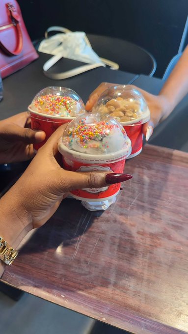 Three hands holding red McDonald's McFlurry cups with colorful sprinkles and nuts, clinking them together in a celebratory toast on a wooden table.
