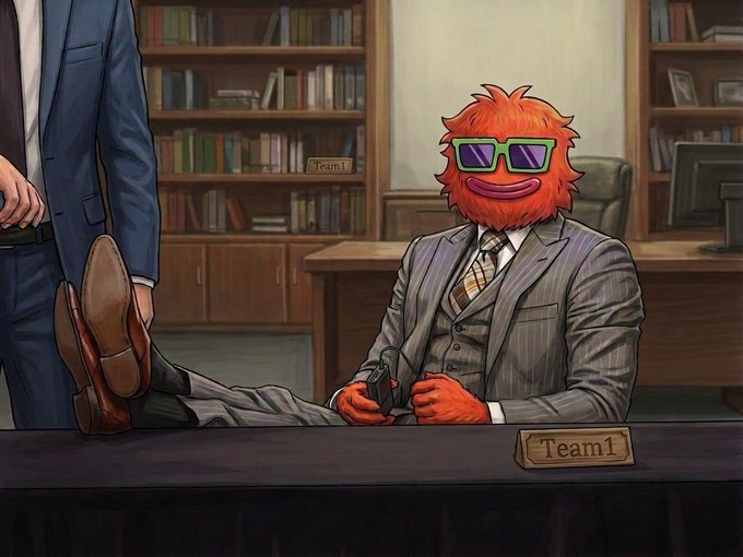 Illustration of an orange furry Muppet-style character wearing a gray pinstripe suit, sunglasses, and tie, sitting at a desk with feet propped up, holding a game controller, with a 'Team1' nameplate in an office with bookshelves.